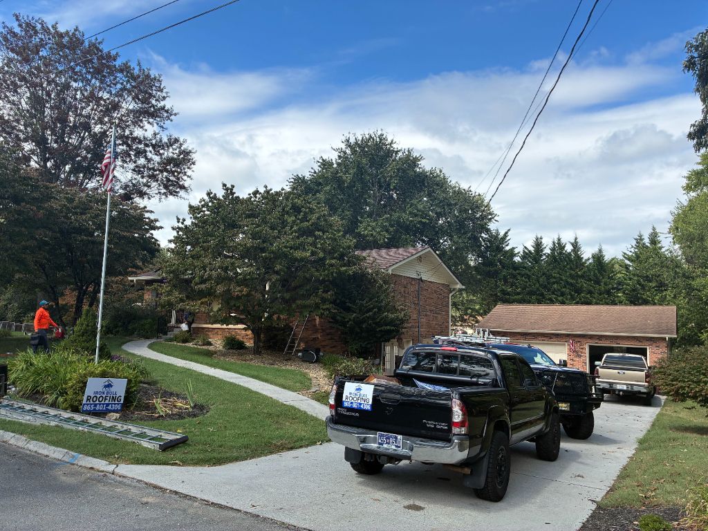 After: completed roof job with Iron Bull Roofing trucks and yard sign parked in the driveway